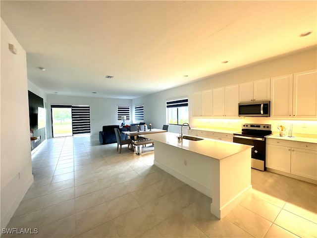 kitchen featuring a kitchen island with sink, sink, range with electric stovetop, light tile patterned floors, and white cabinetry