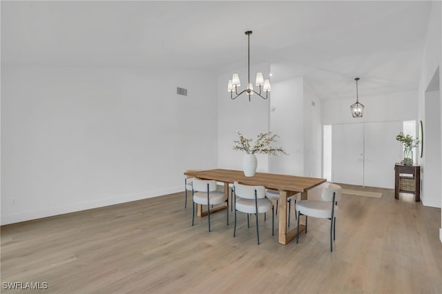 dining room with a notable chandelier, light hardwood / wood-style floors, and vaulted ceiling