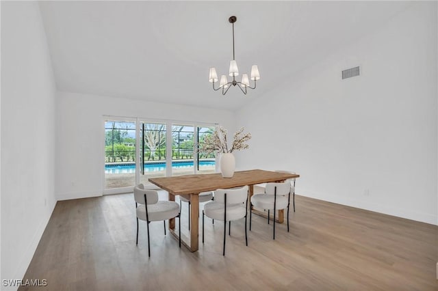 dining room featuring a chandelier, wood finished floors, visible vents, baseboards, and vaulted ceiling