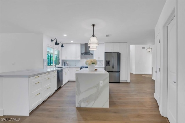 kitchen featuring light wood finished floors, white cabinets, wall chimney exhaust hood, stainless steel appliances, and a sink