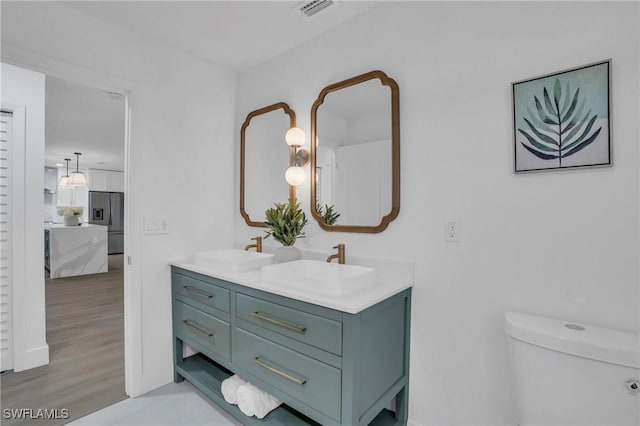 bathroom with double vanity, visible vents, connected bathroom, wood finished floors, and a sink