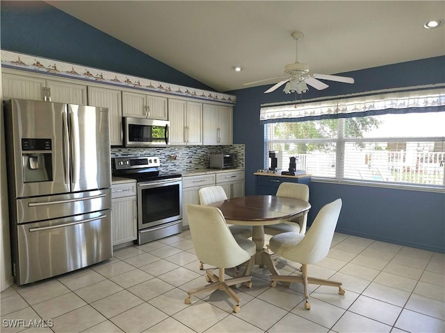 kitchen featuring light tile patterned floors, vaulted ceiling, stainless steel appliances, light countertops, and backsplash