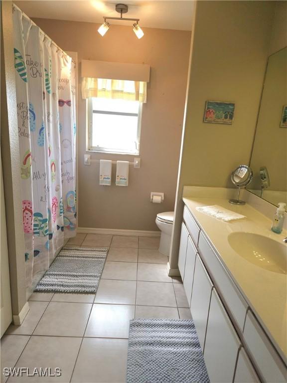 full bath featuring curtained shower, tile patterned flooring, toilet, vanity, and baseboards