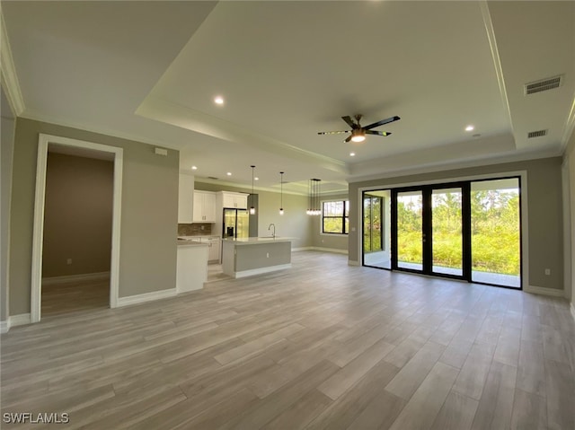 unfurnished living room with ceiling fan, a raised ceiling, sink, crown molding, and light hardwood / wood-style floors