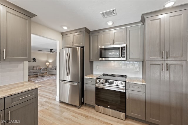 kitchen featuring light hardwood / wood-style floors, stainless steel appliances, backsplash, light stone countertops, and ceiling fan