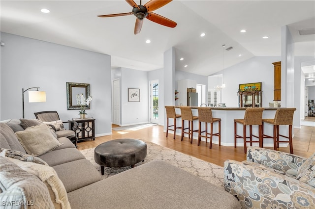 living room with ceiling fan with notable chandelier, lofted ceiling, and light hardwood / wood-style flooring