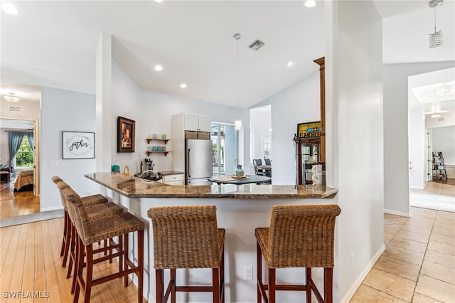 kitchen with pendant lighting, kitchen peninsula, a kitchen bar, and stainless steel fridge