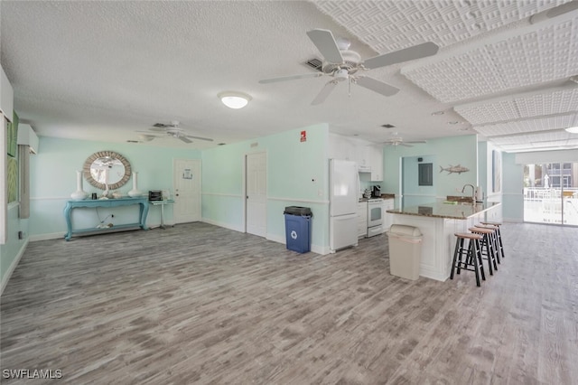 kitchen featuring light wood-type flooring, white cabinets, a kitchen bar, a center island with sink, and white appliances