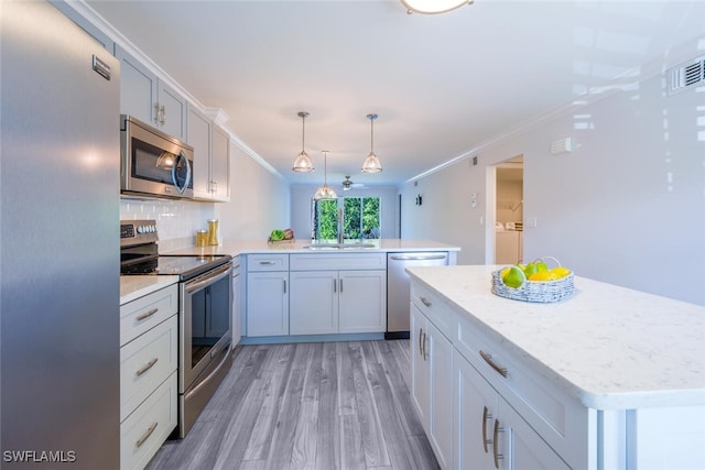 kitchen featuring pendant lighting, crown molding, kitchen peninsula, and appliances with stainless steel finishes