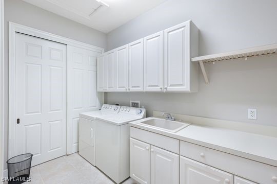 laundry area featuring separate washer and dryer, sink, light tile patterned floors, and cabinets