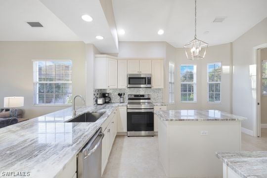 kitchen featuring backsplash, light stone counters, stainless steel appliances, sink, and hanging light fixtures