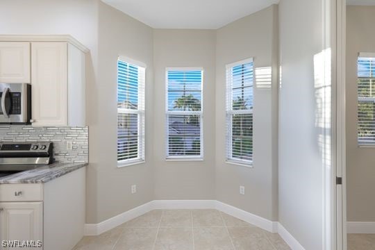 kitchen with white cabinets, appliances with stainless steel finishes, tasteful backsplash, and light stone counters