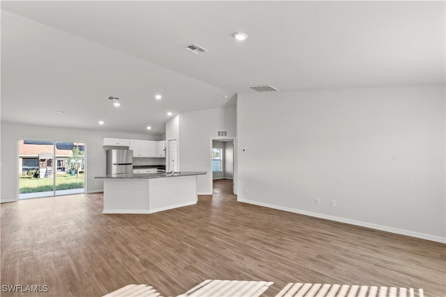 kitchen featuring stainless steel fridge, dark stone counters, vaulted ceiling, light hardwood / wood-style flooring, and white cabinetry