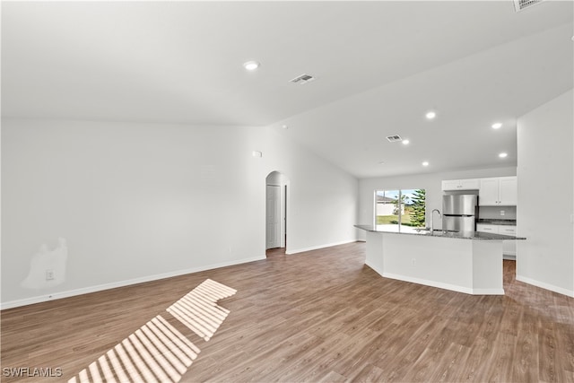 unfurnished living room featuring light wood-type flooring, vaulted ceiling, and sink