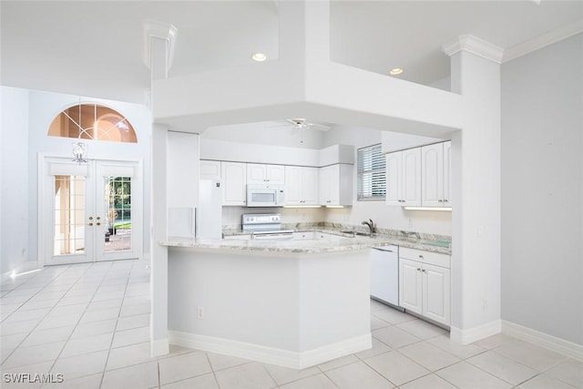 kitchen featuring a peninsula, white appliances, a sink, white cabinetry, and light stone countertops