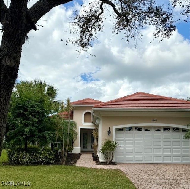 mediterranean / spanish-style home with a garage, a tiled roof, decorative driveway, french doors, and stucco siding