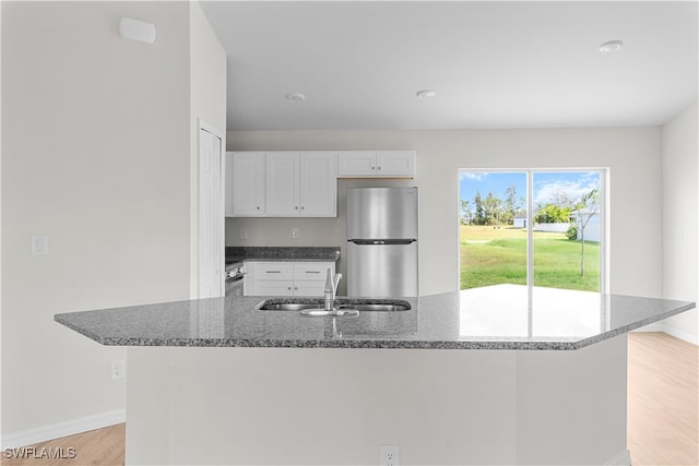 kitchen featuring sink, white cabinetry, stainless steel appliances, dark stone counters, and light hardwood / wood-style flooring