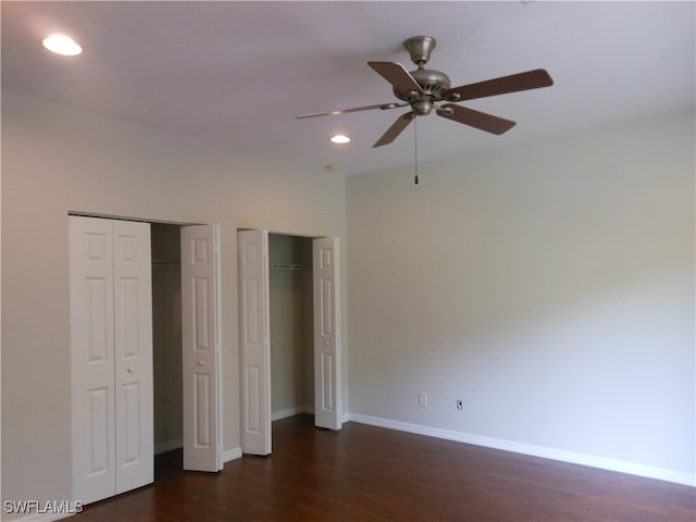 unfurnished bedroom featuring ceiling fan, multiple closets, and dark wood-type flooring