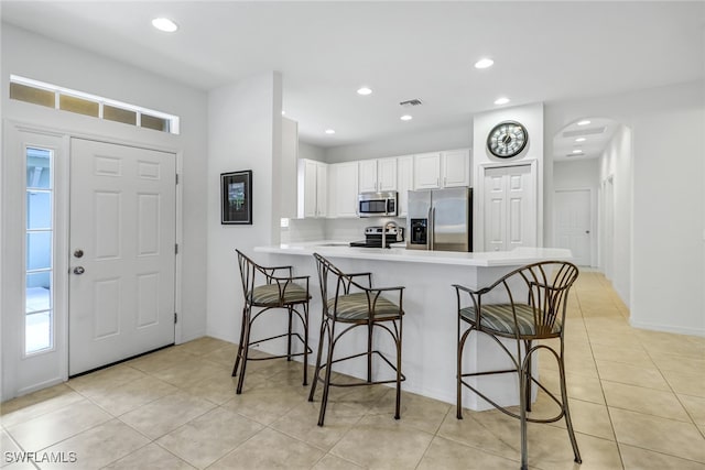 kitchen featuring visible vents, white cabinets, a breakfast bar area, a peninsula, and stainless steel appliances