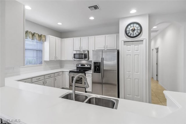 kitchen featuring stainless steel appliances, white cabinetry, a sink, arched walkways, and light countertops