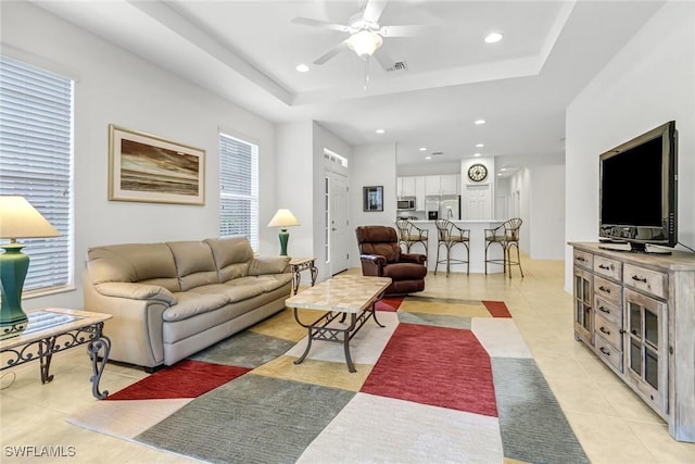 living area with ceiling fan, a tray ceiling, recessed lighting, and light tile patterned floors
