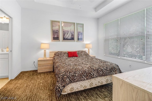 carpeted bedroom with a tray ceiling, baseboards, and ensuite bath