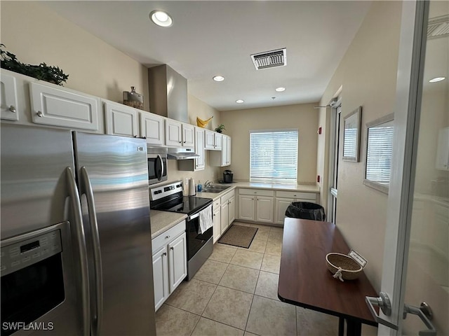kitchen with stainless steel appliances, light countertops, white cabinetry, light tile patterned floors, and under cabinet range hood