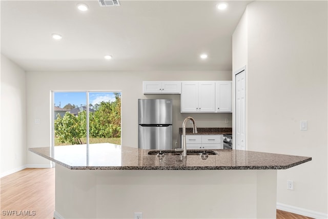 kitchen with dark stone countertops, sink, stainless steel fridge, white cabinets, and light hardwood / wood-style floors