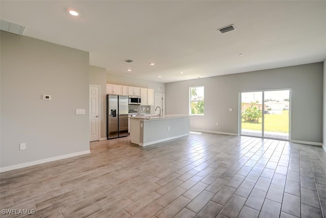 kitchen with appliances with stainless steel finishes, white cabinetry, light hardwood / wood-style flooring, a center island with sink, and sink