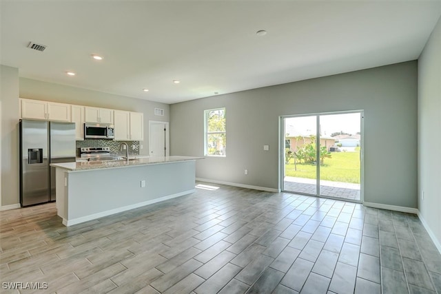 kitchen with light hardwood / wood-style floors, white cabinetry, an island with sink, stainless steel appliances, and sink