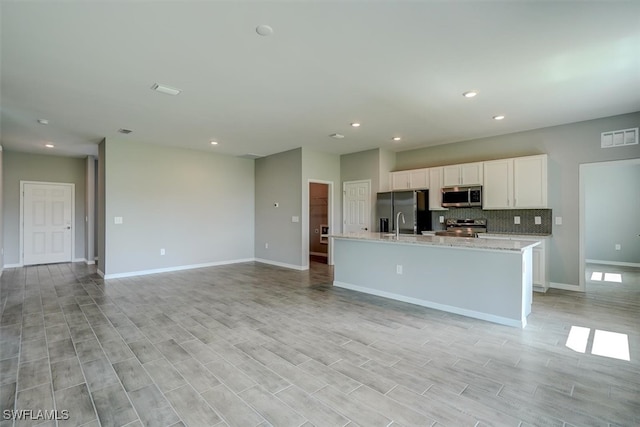 kitchen with appliances with stainless steel finishes, light stone counters, white cabinets, light hardwood / wood-style flooring, and a kitchen island with sink