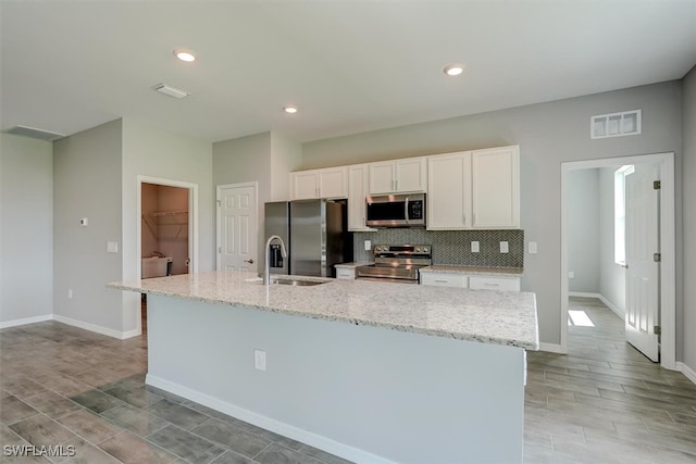 kitchen with stainless steel appliances, white cabinetry, a center island with sink, and sink