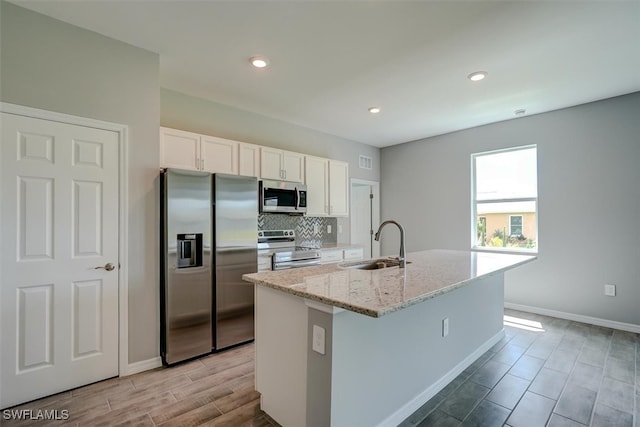 kitchen with light stone counters, white cabinets, an island with sink, sink, and stainless steel appliances