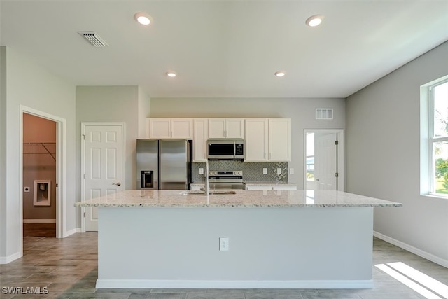 kitchen with an island with sink, stainless steel appliances, white cabinetry, and light stone countertops