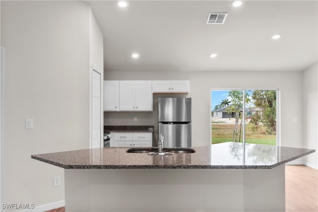 kitchen with white cabinetry, dark stone countertops, stainless steel refrigerator, and light wood-type flooring