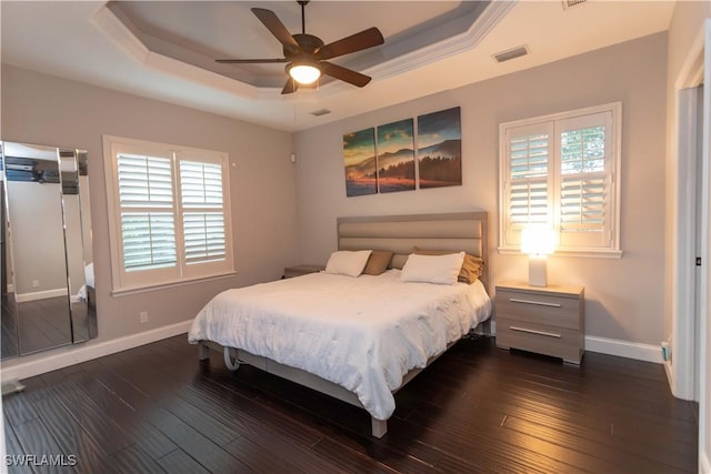 bedroom with a raised ceiling, ceiling fan, dark wood-type flooring, and multiple windows