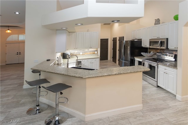 kitchen featuring kitchen peninsula, appliances with stainless steel finishes, backsplash, and white cabinetry