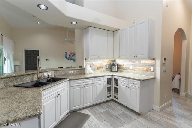 kitchen featuring sink, white cabinetry, tasteful backsplash, light stone countertops, and kitchen peninsula