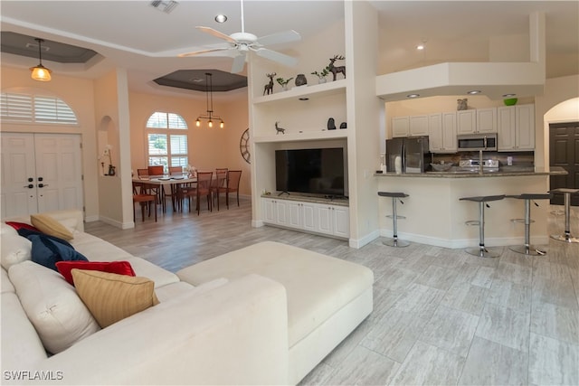 living room featuring a raised ceiling, ceiling fan, light hardwood / wood-style floors, and a high ceiling