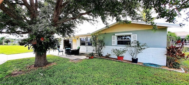 view of front facade with stucco siding, a patio, and a front yard