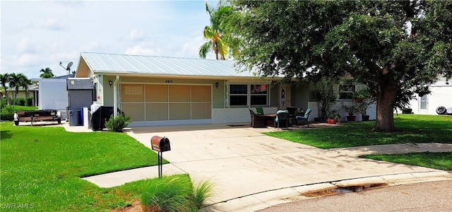 ranch-style home featuring an attached carport, driveway, metal roof, and a front yard