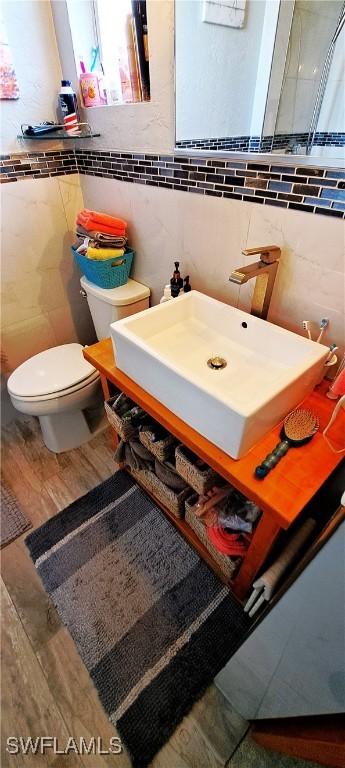 bathroom featuring vanity, toilet, tile walls, and wood finished floors