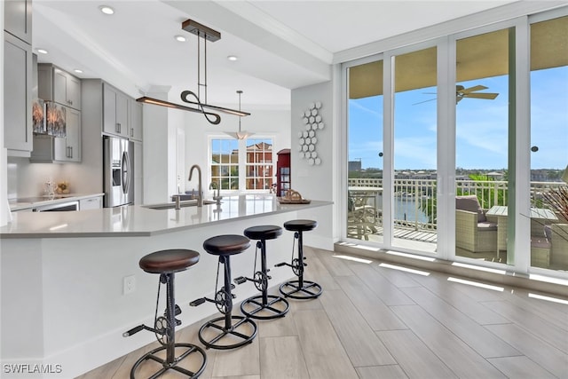 kitchen with stainless steel refrigerator with ice dispenser, sink, a breakfast bar, gray cabinets, and a water view