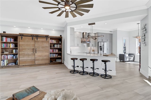 kitchen with a kitchen bar, a barn door, kitchen peninsula, hanging light fixtures, and stainless steel fridge with ice dispenser