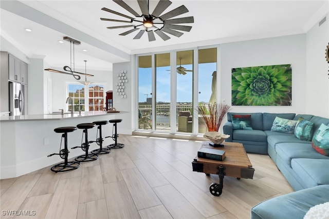 living room featuring crown molding, sink, light wood-type flooring, and ceiling fan