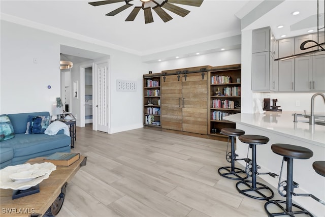 living room with sink, ceiling fan, light hardwood / wood-style flooring, and a barn door