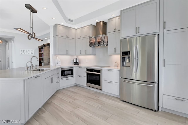 kitchen featuring kitchen peninsula, sink, pendant lighting, wall chimney exhaust hood, and stainless steel appliances