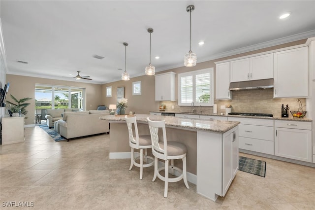 kitchen featuring hanging light fixtures, white cabinetry, a kitchen island, black gas stovetop, and under cabinet range hood