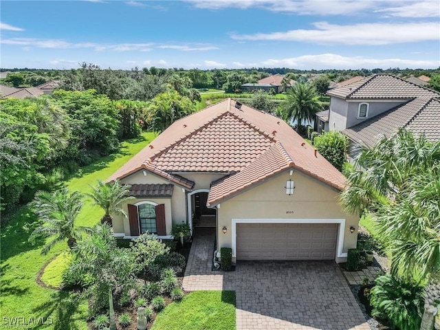 mediterranean / spanish-style home featuring decorative driveway, a tiled roof, an attached garage, and stucco siding