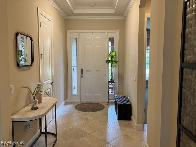 entrance foyer featuring light tile patterned floors, a raised ceiling, baseboards, and ornamental molding